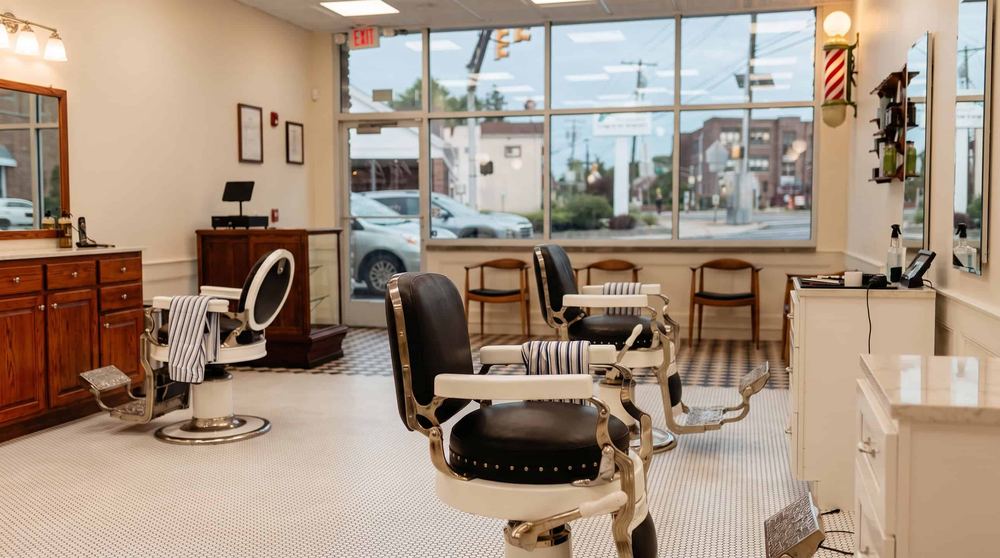 Barber chairs facing the front window at Per Lui Barbershop, with Main Street visible outside.
